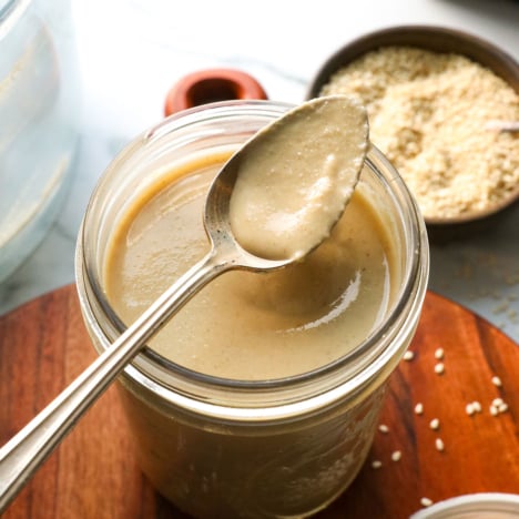 a spoon with homemade tahini sitting on a glass jar with more tahini.