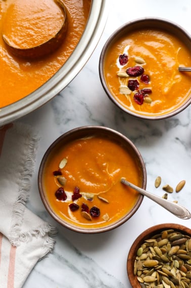 slow cooker pumpkin soup in two bowls with cranberries on top.