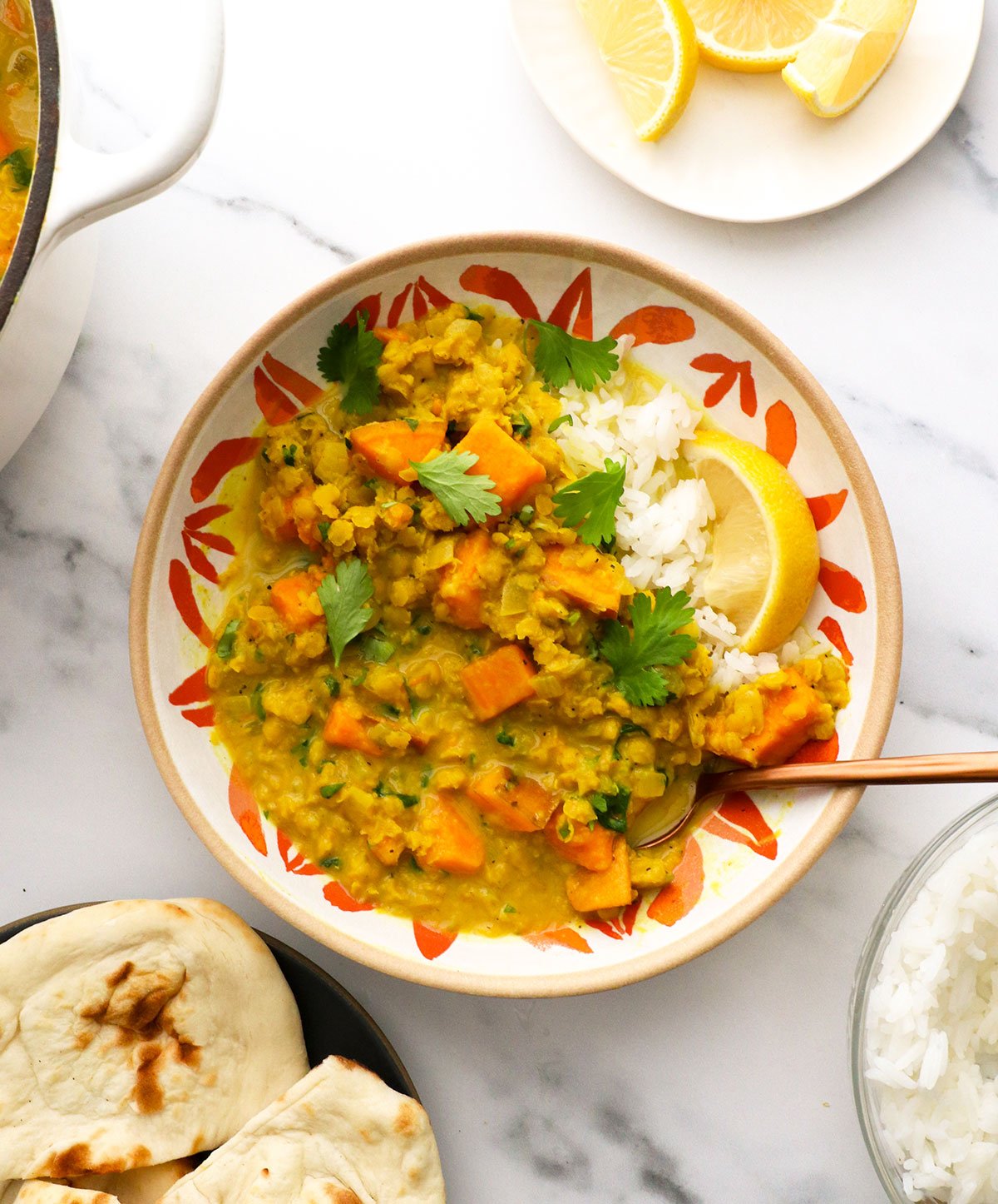 red lentil and sweet potato curry served over rice in a bowl with a spoon. 