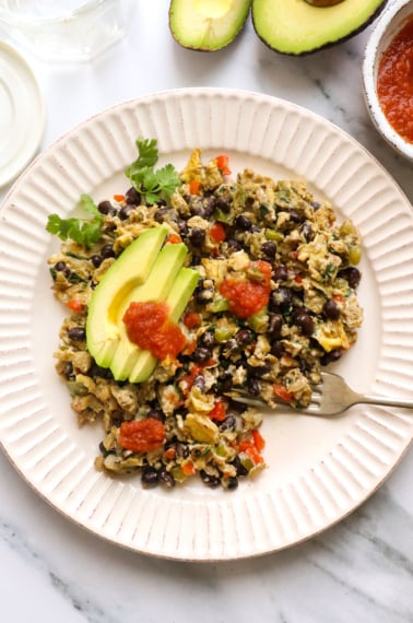high protein breakfast scramble on a plate topped with avocado slices.