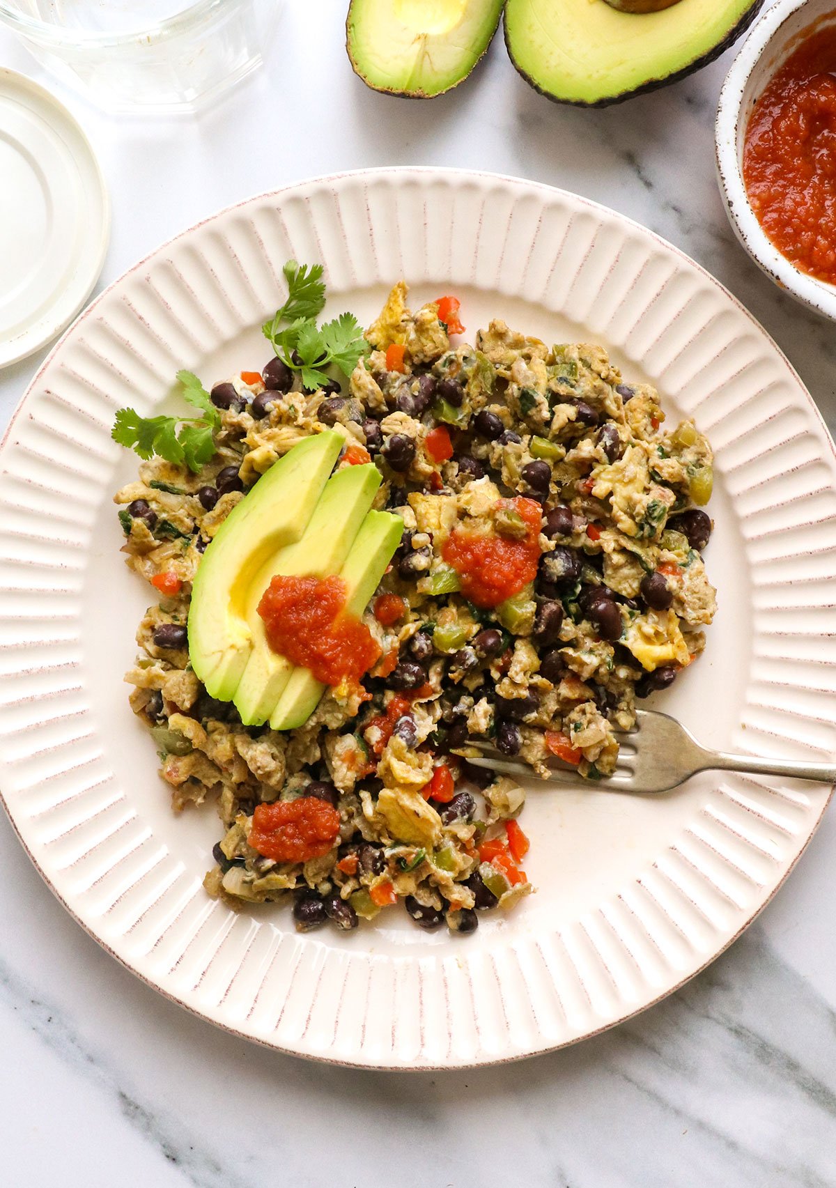 high protein breakfast scramble on a plate topped with avocado slices.