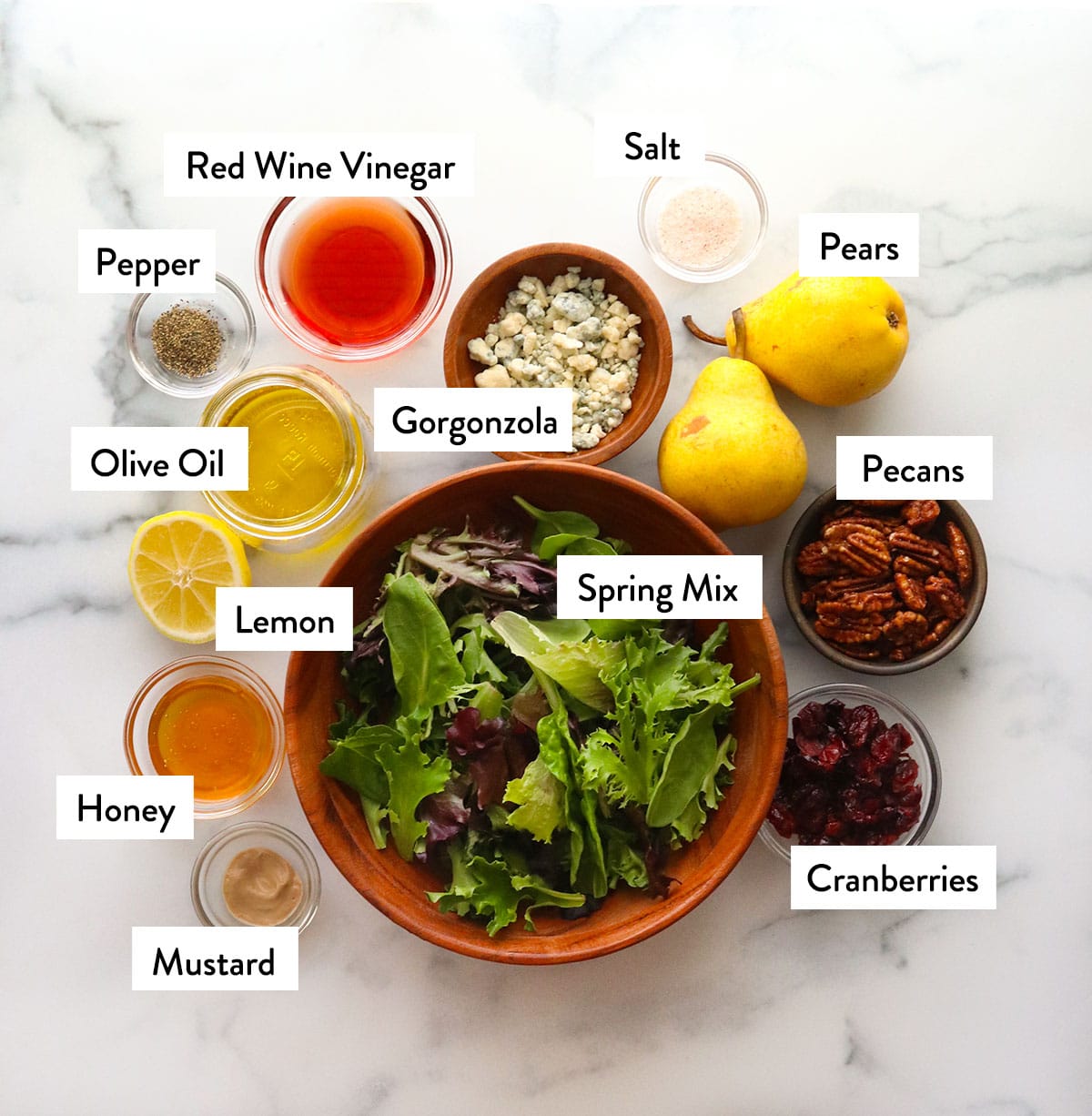 bowl of spring mix, fresh pears, cranberries, pecans, and gorgonzola cheese on a white surface.