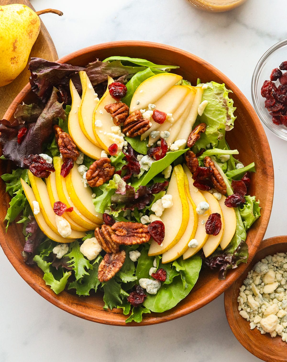 bed of spring mix in a bowl topped with sliced pears, cranberries, pecans, and gorgonzola.