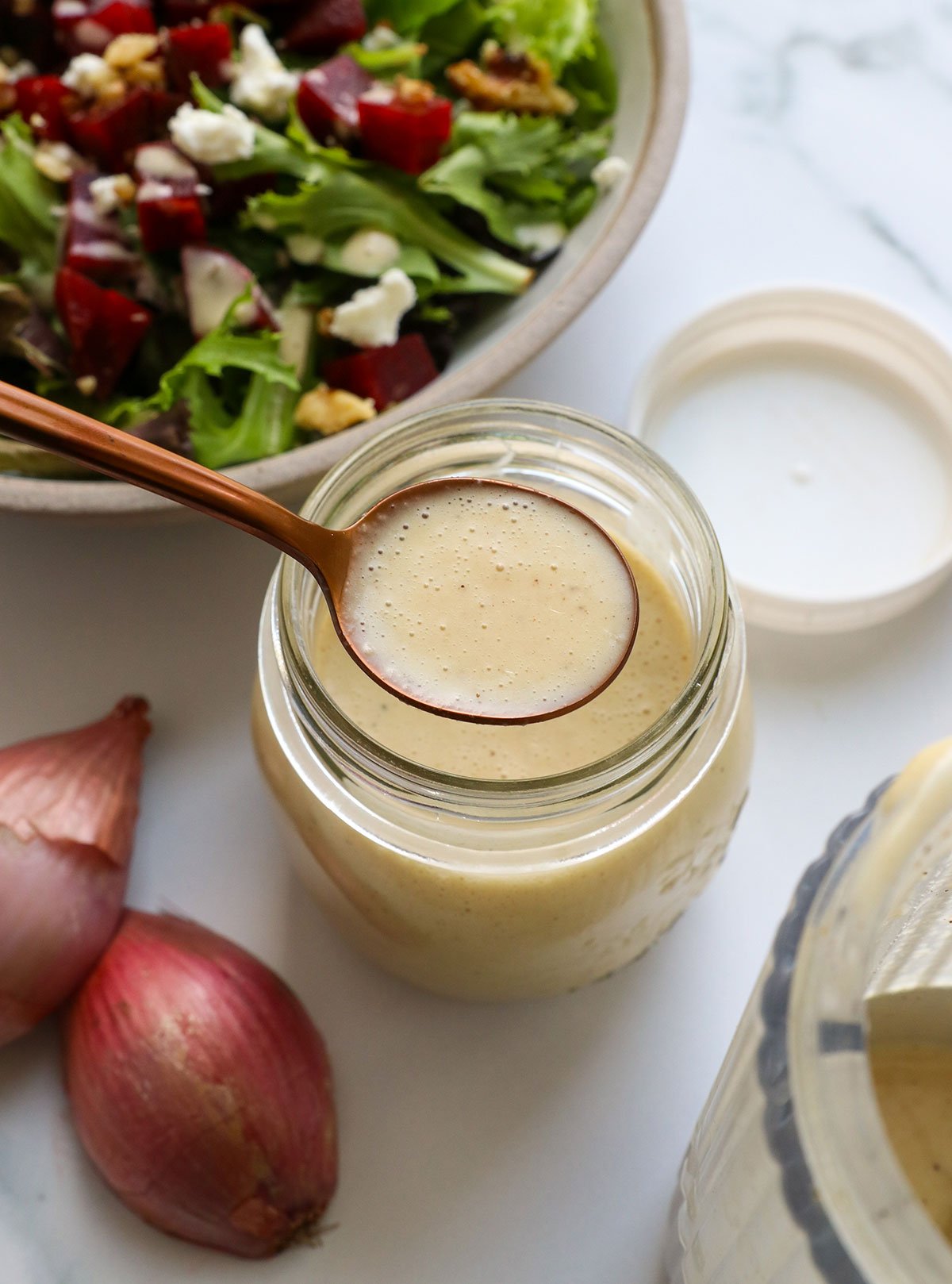 shallot vinagirette on a spoon over a glass jar of dressing.