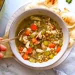 chicken and lentil soup served with bread on the side and a spoon.