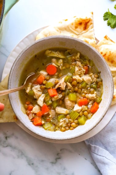 chicken and lentil soup served with bread on the side and a spoon.