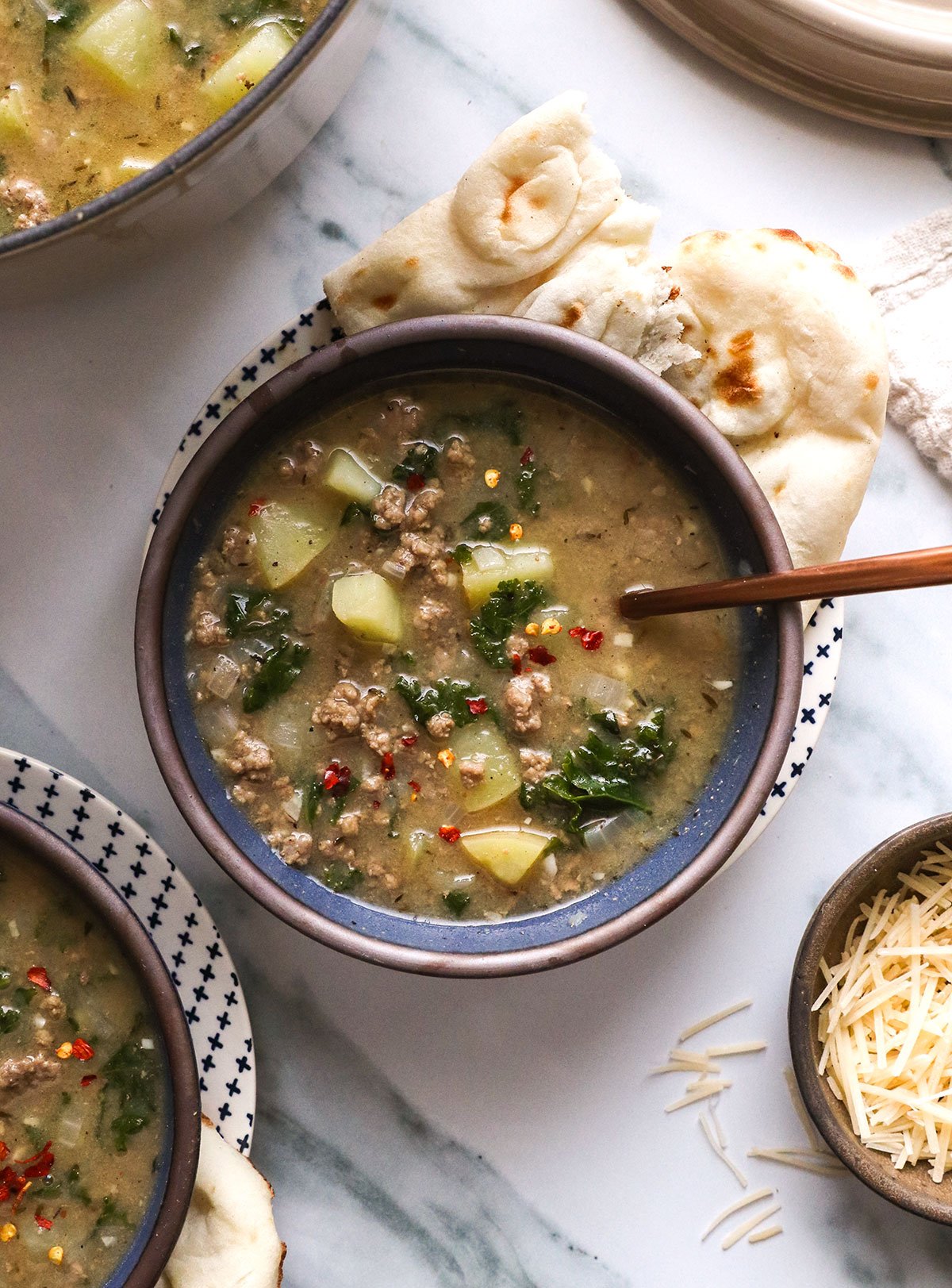 two bowls of healthy zuppa toscana served with red pepper flakes on top.
