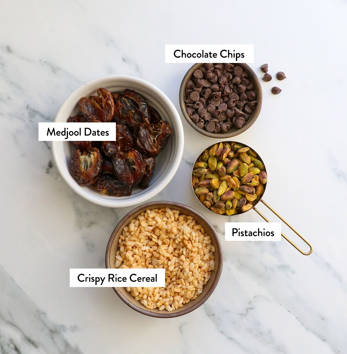 dates, rice cereal, chocolate chips, and pistachios labeled in bowls.