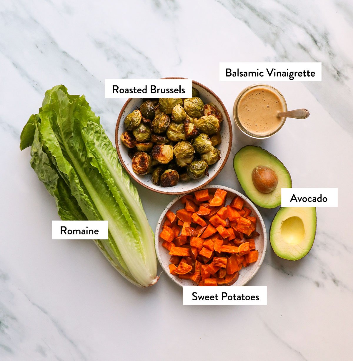 romaine, brussels sprouts, sweet potatoes, avocado, and balsamic vinaigrette labeled on a white surface. 