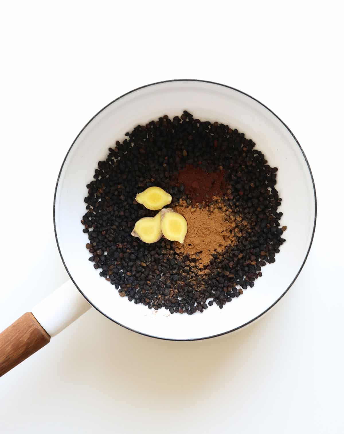 dried elderberries, ginger, cinnamon and cloves added to a white saucepan.