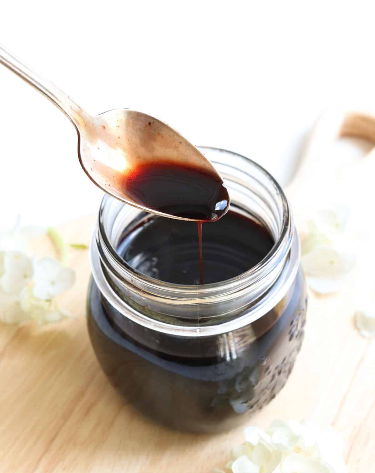 homemade elderberry syrup pouring from a spoon to show the consistency.