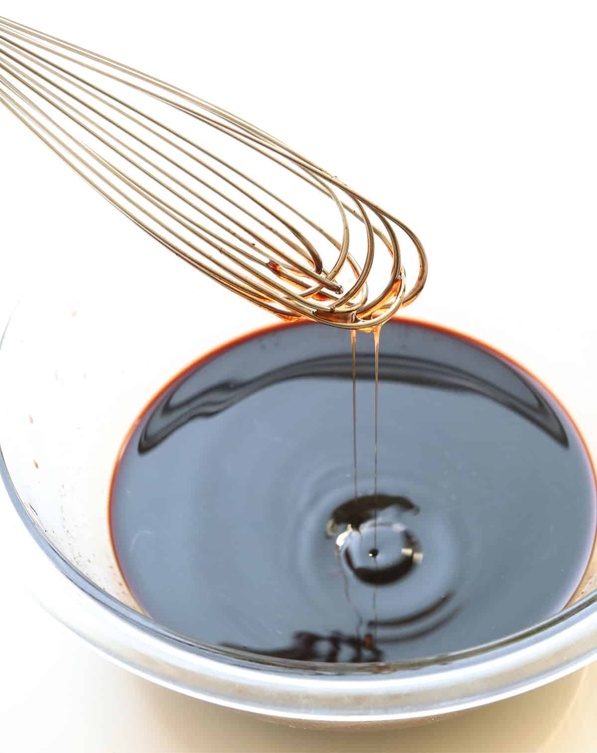 honey dripping off of a whisk after stirring it into the elderberry syrup.