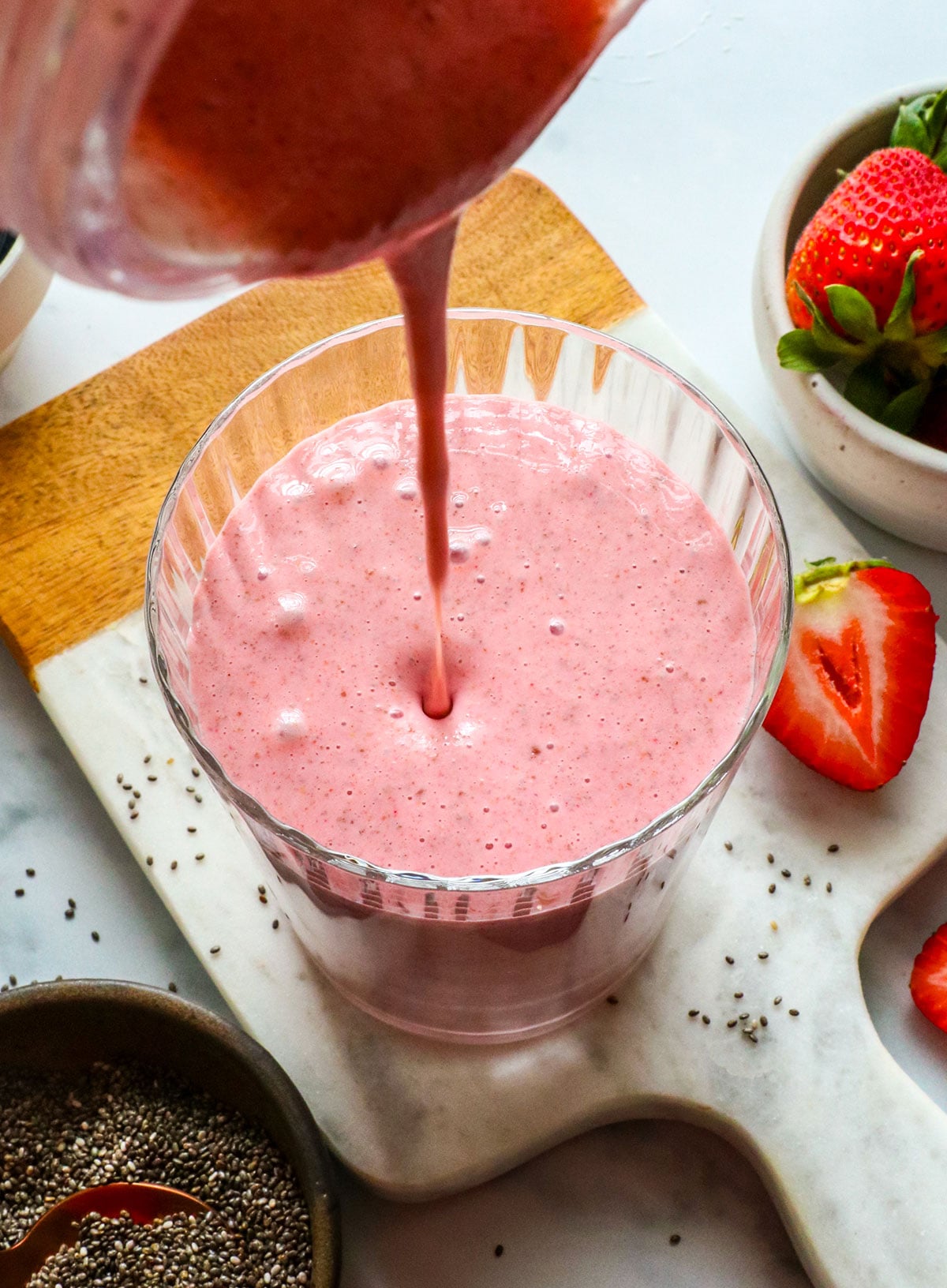 chia seed smoothie poured into a glass with strawberries nearby.