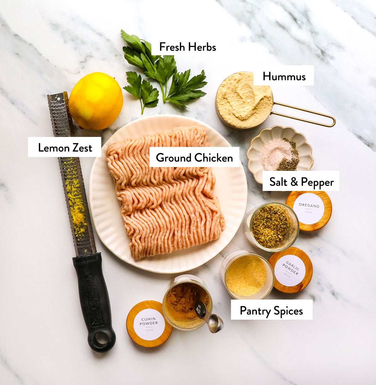 ground chicken, spices, lemon zest, and hummus labeled on a white surface.