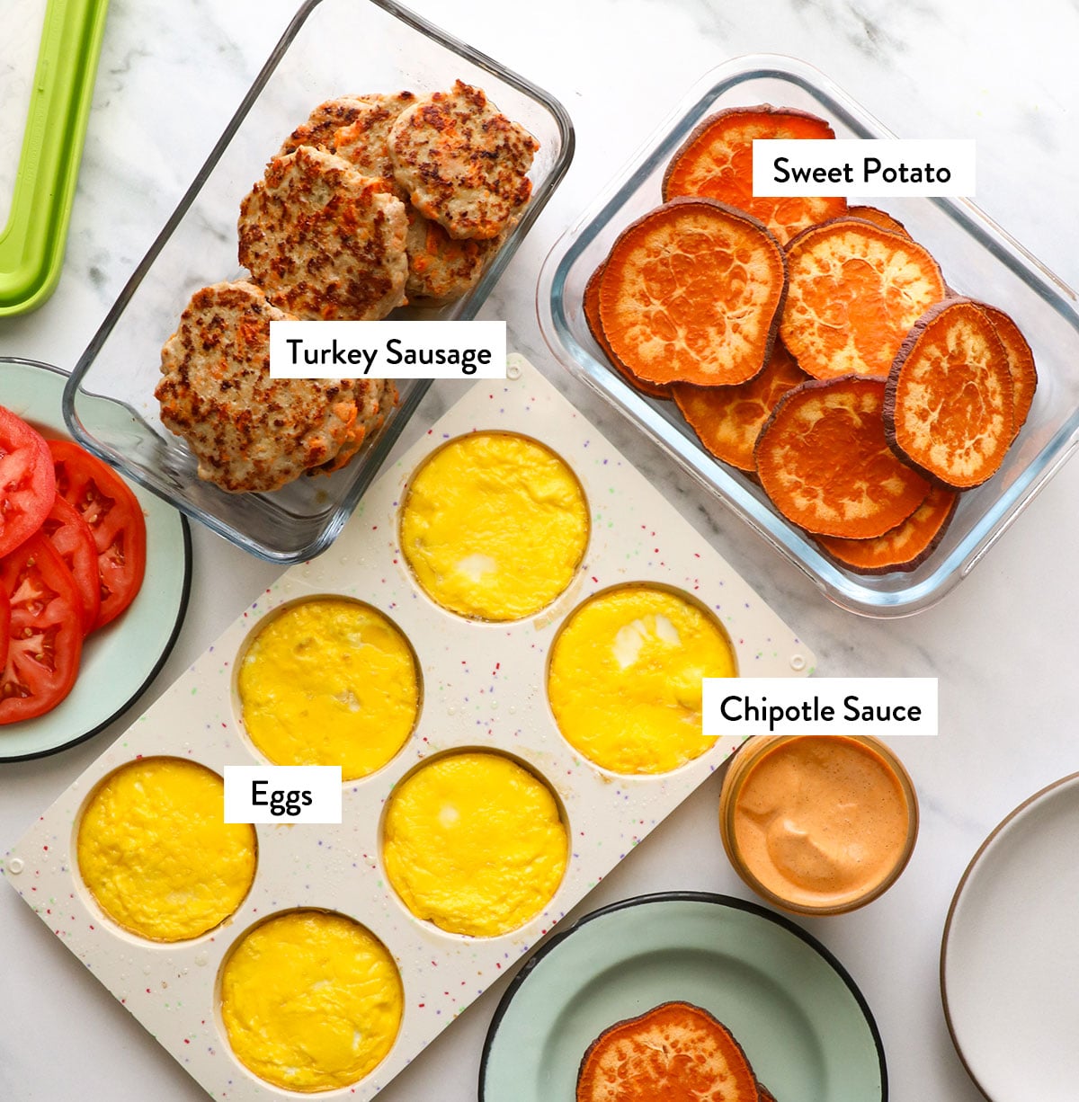 baked eggs, sweet potato slices, turkey sausage, and a jar of chipotle sauce on a white surface.