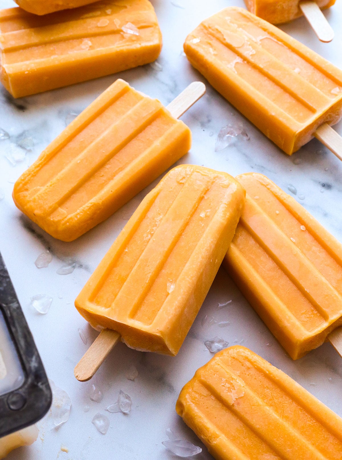 peach popsicles on a marble surface with ice.