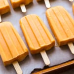 peach popsicles on a parchment lined pan.