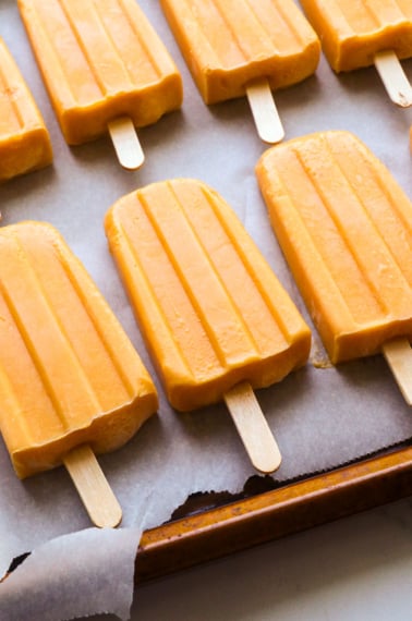 peach popsicles on a parchment lined pan.