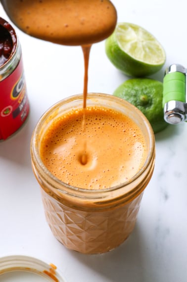 spoon dripping chipotle sauce into a glass jar.