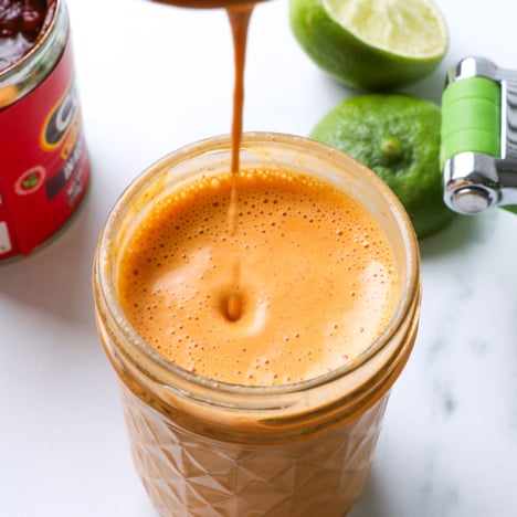 spoon dripping chipotle sauce into a glass jar.