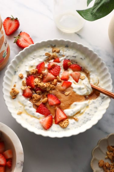white bowl filled with greek yogurt, chia seeds, peanut butter, and fruit.