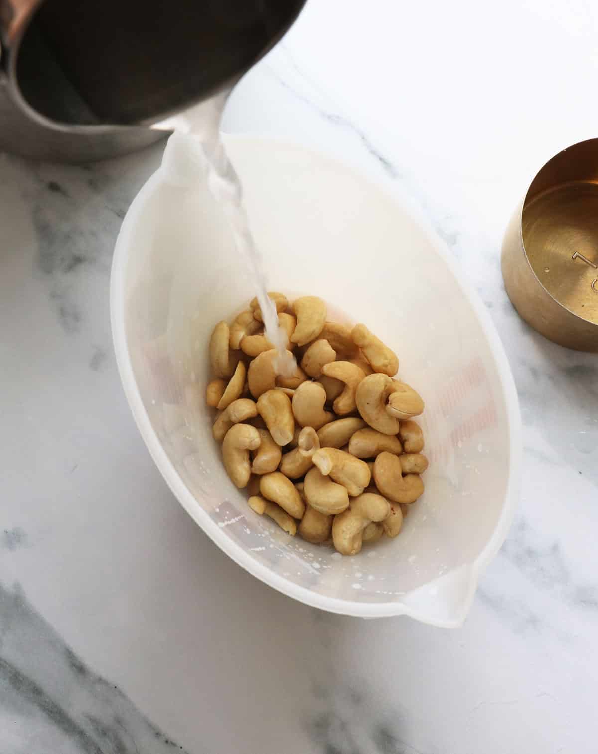 hot water poured over cashews in a measuring cup.