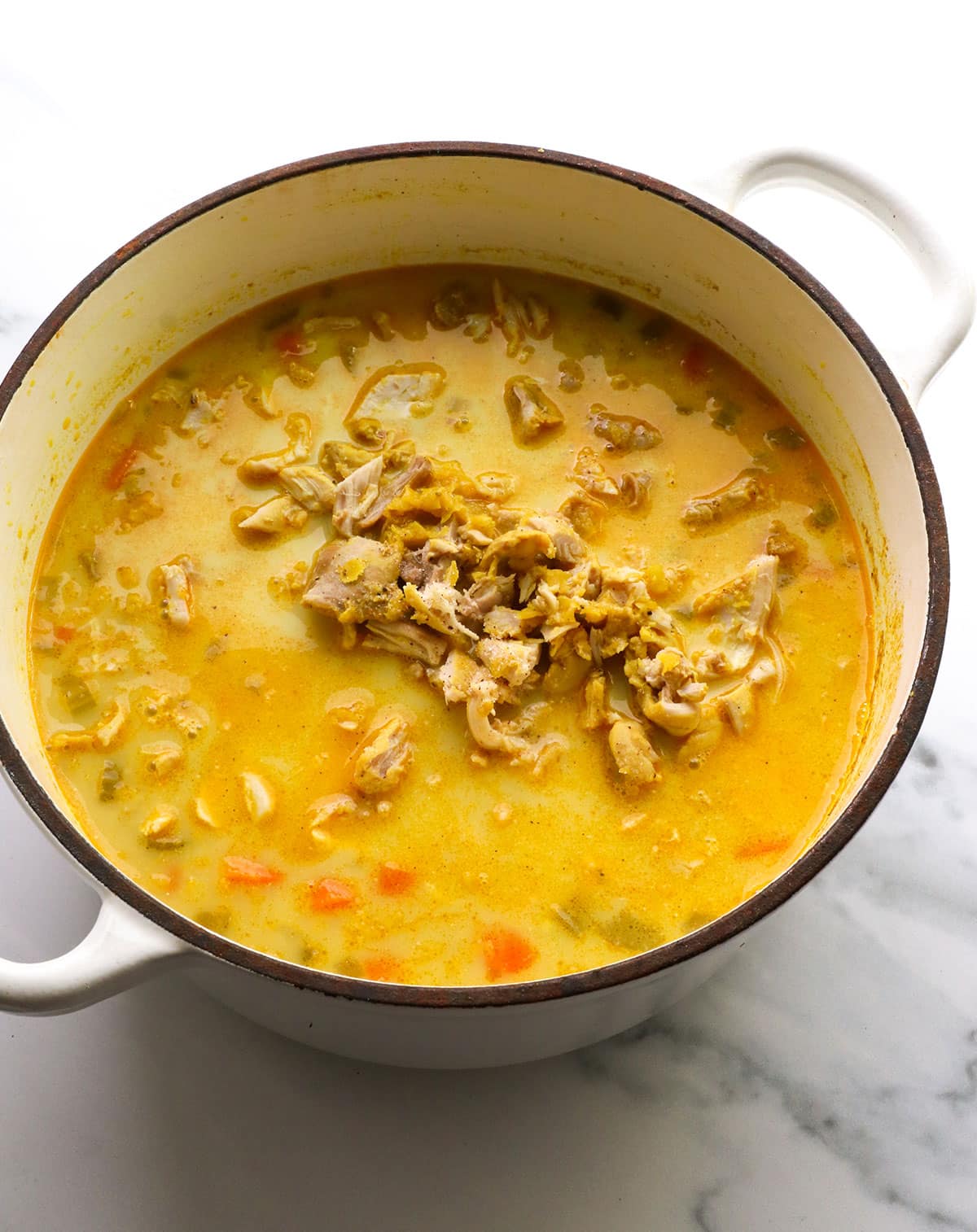 chicken added to curry soup in a white pot.