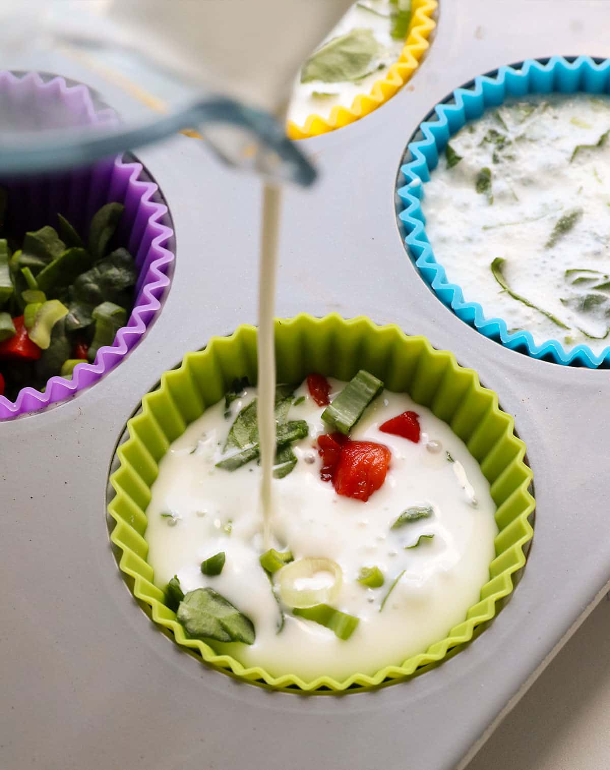egg white mixture poured over veggies in a muffin pan.