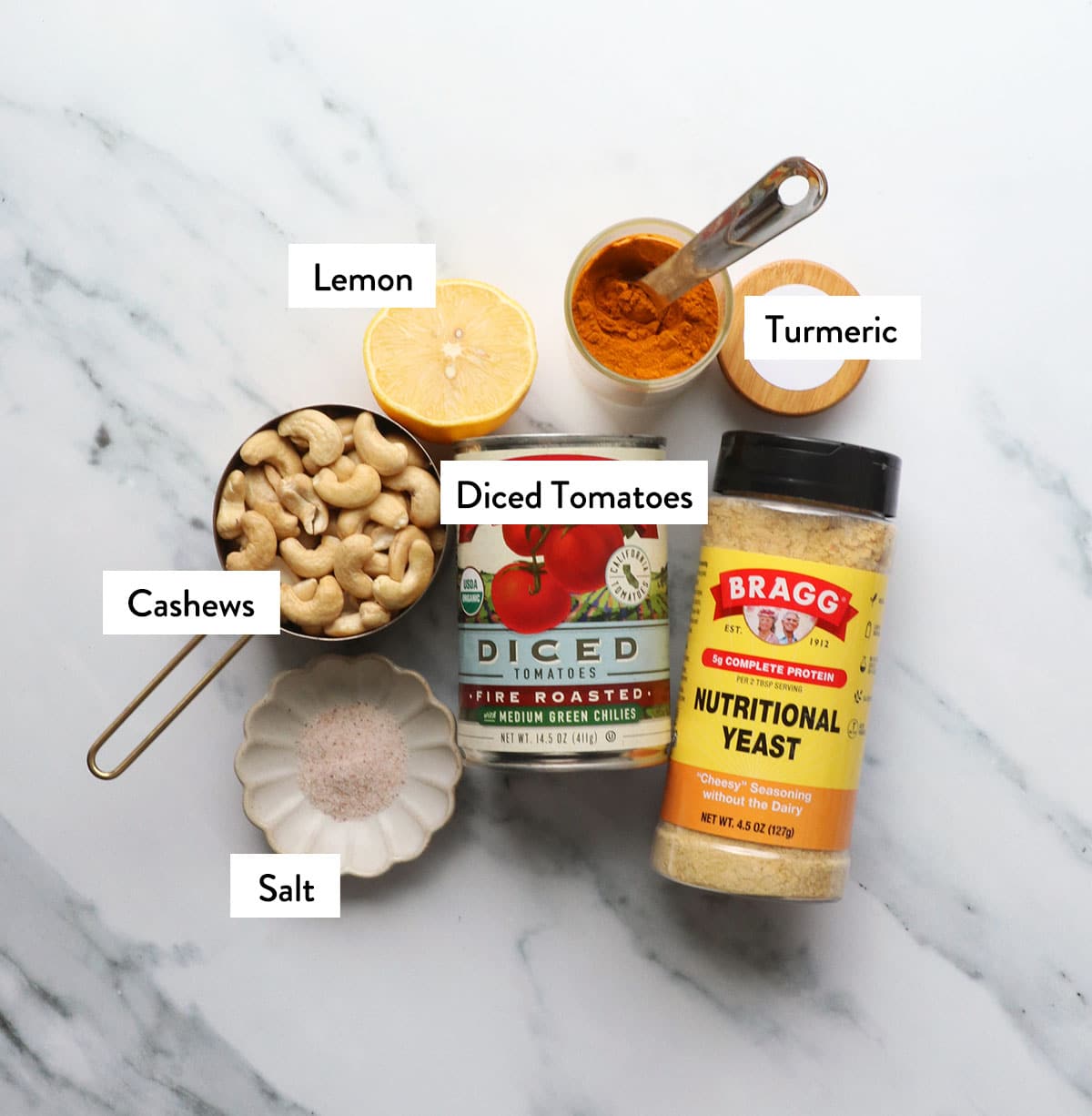 nutritional yeast, cashews, diced tomatoes can, and spices on a white surface.