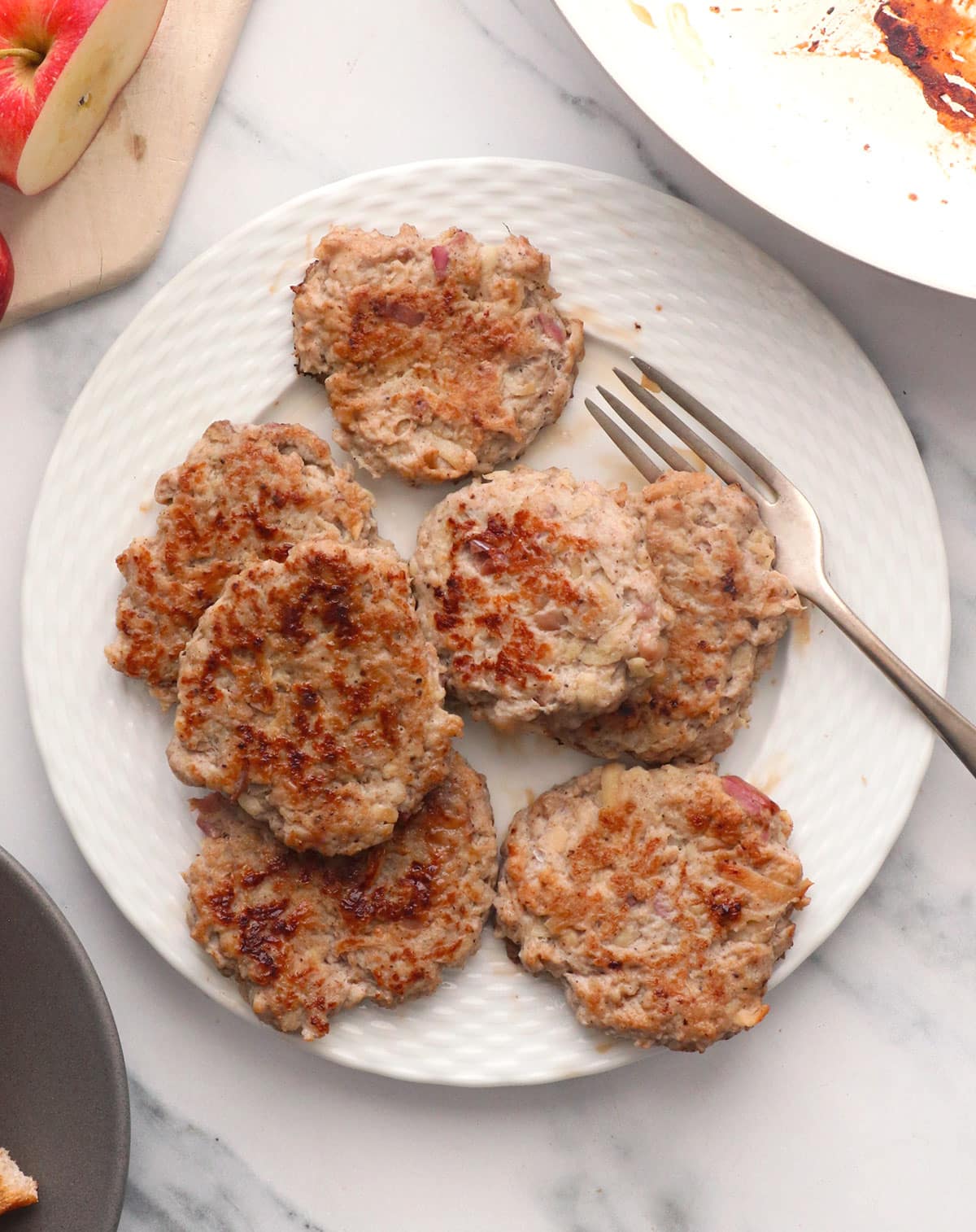 chicken apple sausages set on a white plate for serving with a fork.