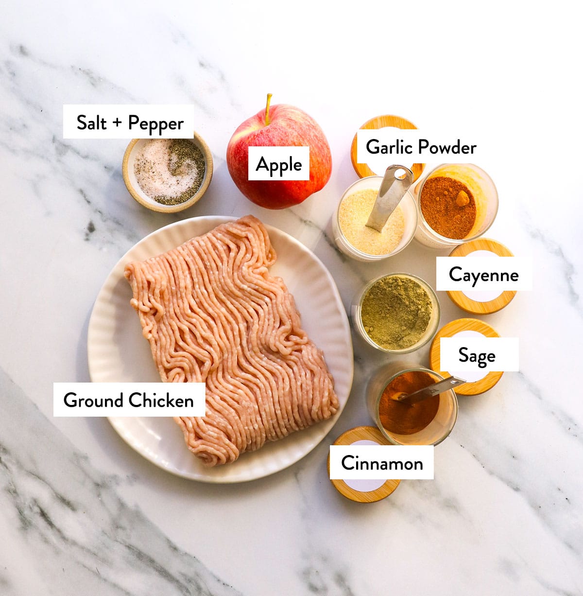 ground chicken on a plate with jars of spices, a fresh apple, and salt and pepper nearby.