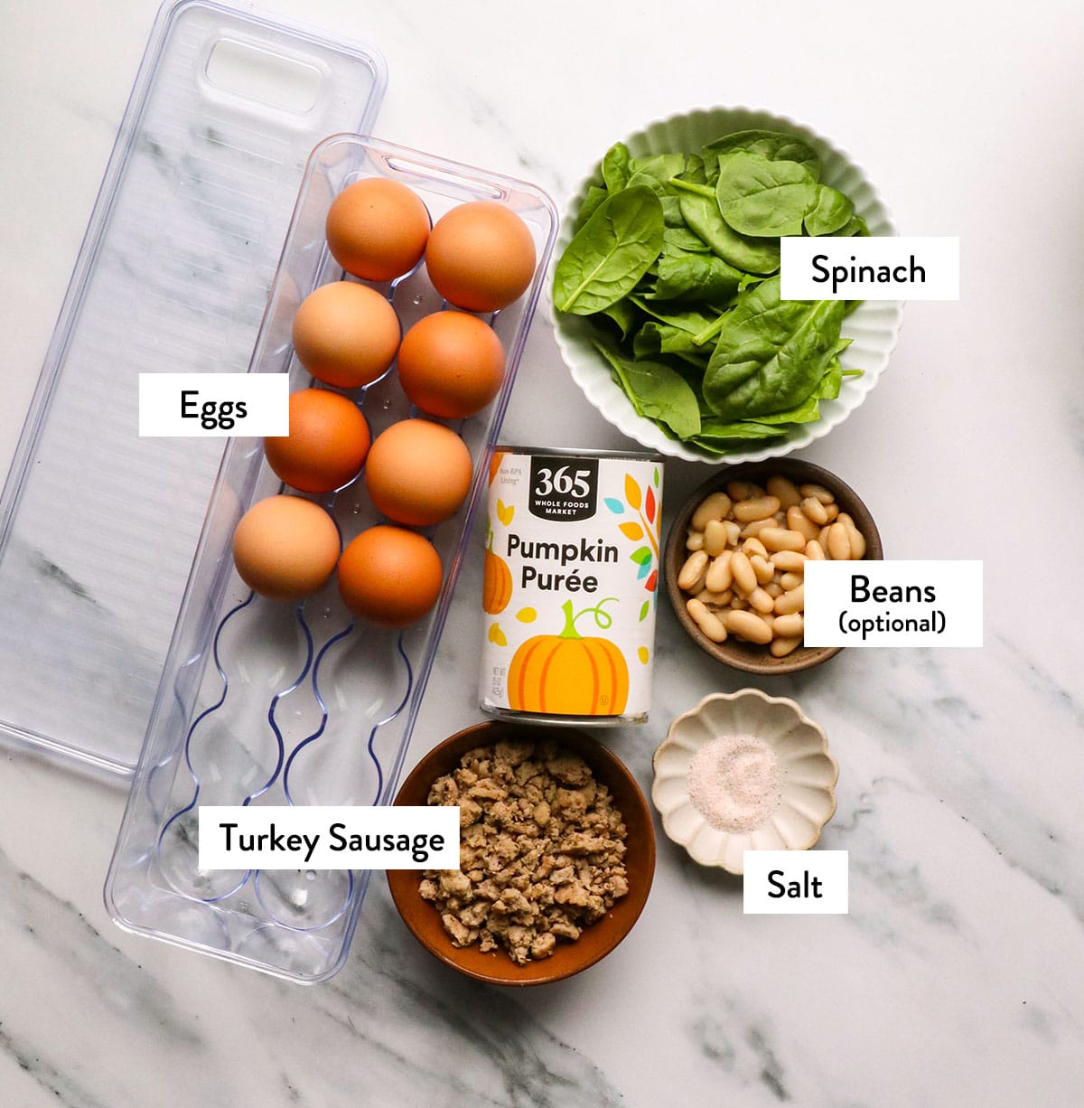 eggs, spinach, italian ground turkey, pumpkin puree and salt in bowls on a white surface.