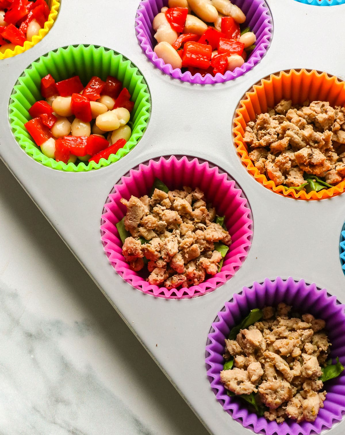ground turkey sausage and white beans added to a muffin pan with silicone liners.