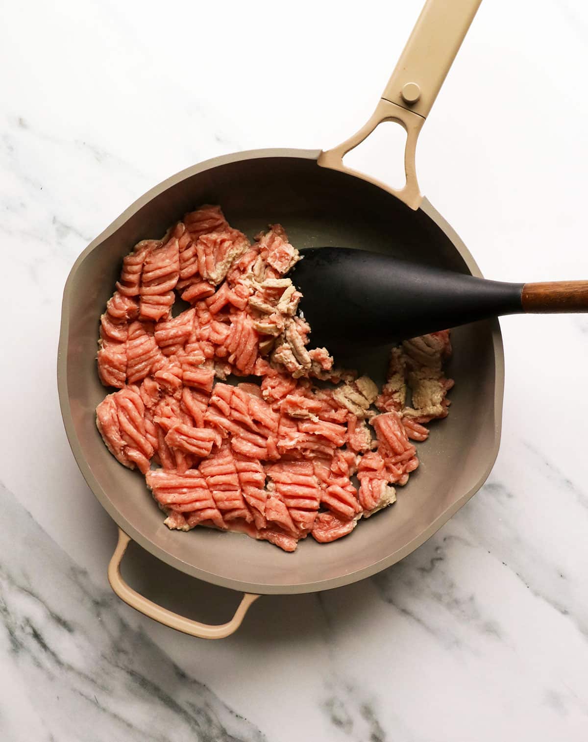 ground turkey starting to cook in a skillet with a sturdy spatula.