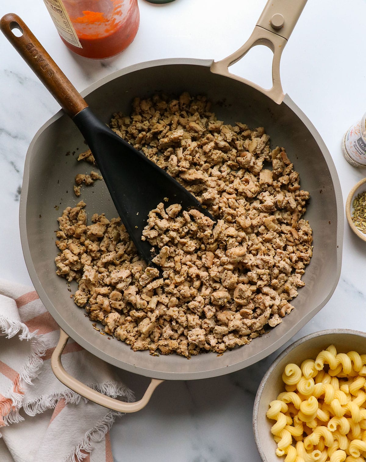 ground turkey sausage in a skillet near pasta and marinara sauce.