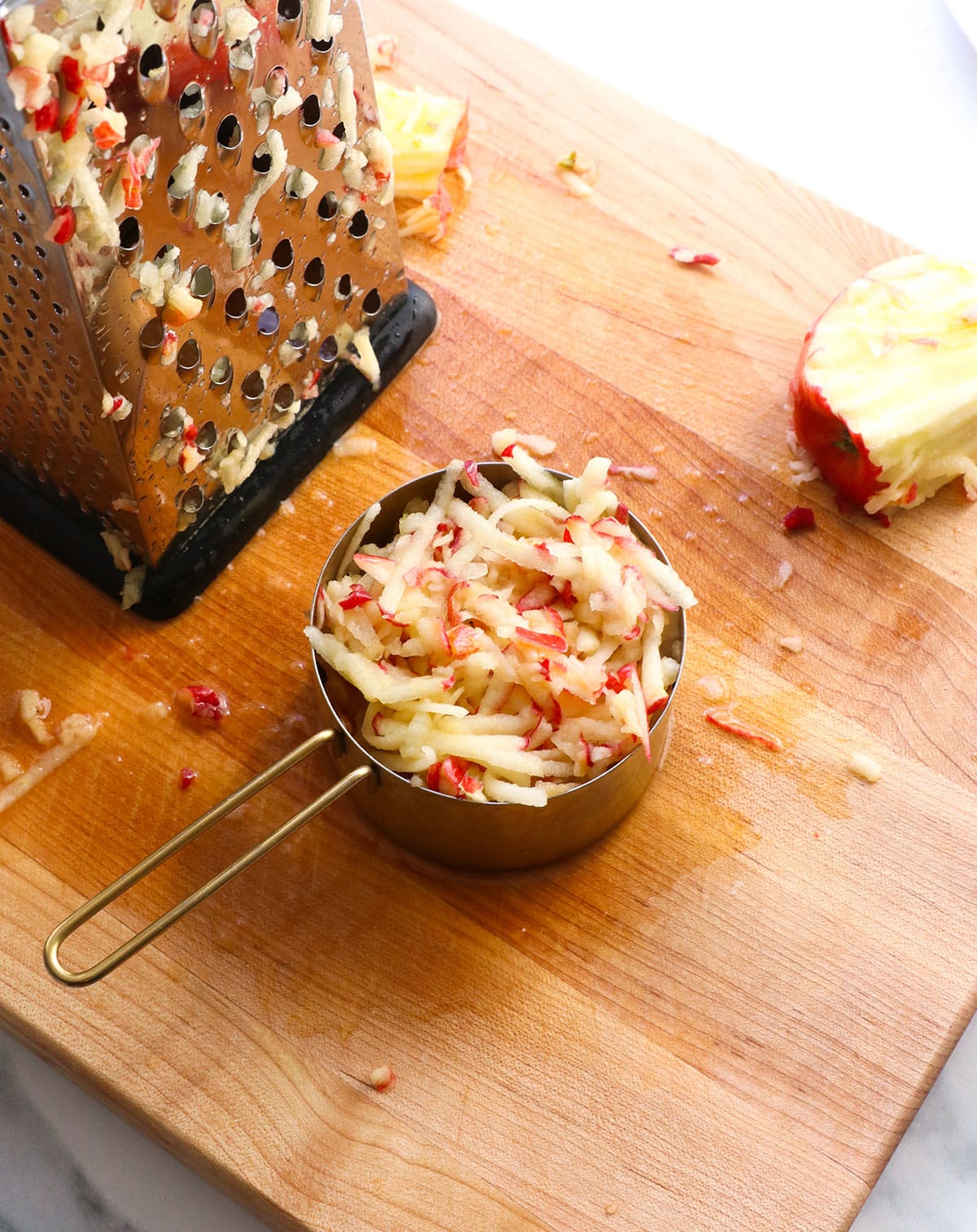 apple shredded on a board and added to a measuring cup.